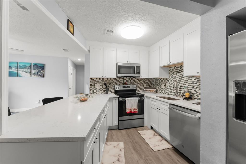 A modern kitchen features white cabinets, stainless steel appliances, and a long quartz countertop island — 1518 DAROCA DRIVE, DELTONA, FL