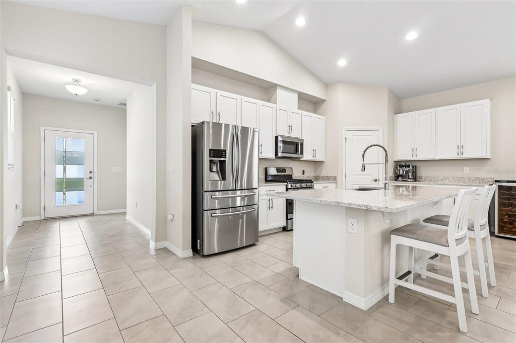 A modern kitchen features white cabinets, stainless steel appliances, a granite island, and tile flooring — 12103 EASTMOOR DRIVE, WINTER GARDEN, FL