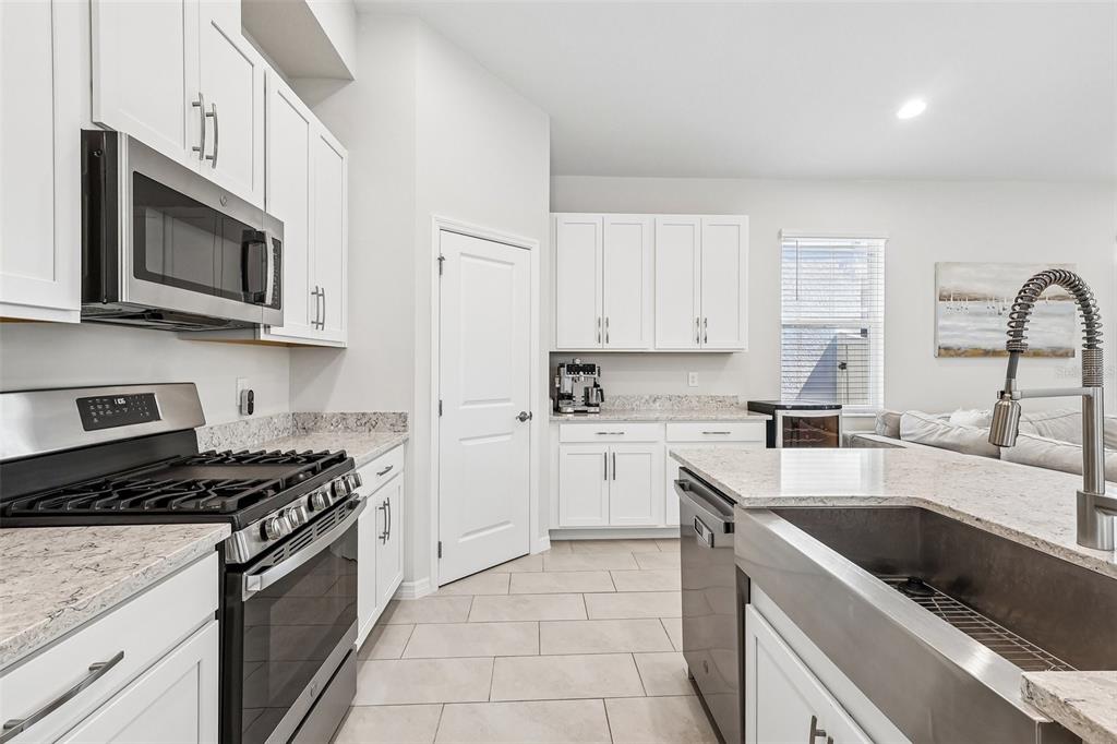 A kitchen features white cabinets, granite countertops, stainless steel appliances, and a farmhouse sink — 12103 EASTMOOR DRIVE, WINTER GARDEN, FL