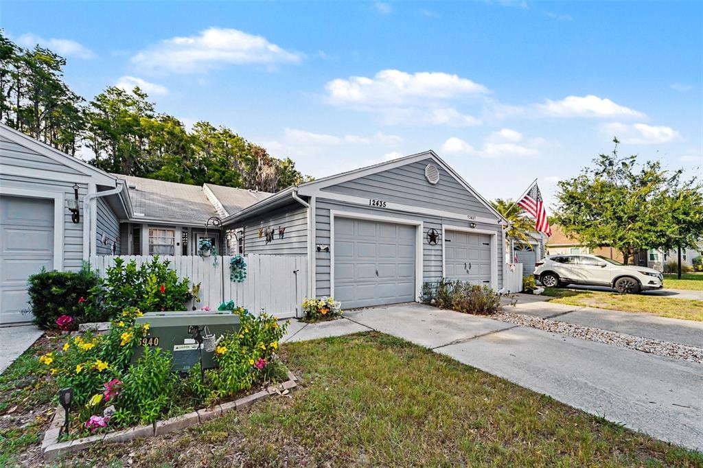 A gray-sided house with two garage doors and a white fence in the front yard — 12435 KNOLLBROOK LANE, HUDSON, FL