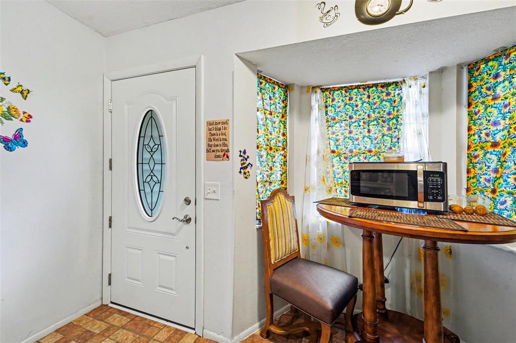 A kitchen corner features a white door, a sunflower-patterned window treatment, and a small table — 12435 KNOLLBROOK LANE, HUDSON, FL