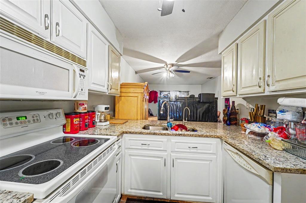 A kitchen features white cabinets, granite countertops, a glass-top stove, and a stainless steel sink — 12435 KNOLLBROOK LANE, HUDSON, FL