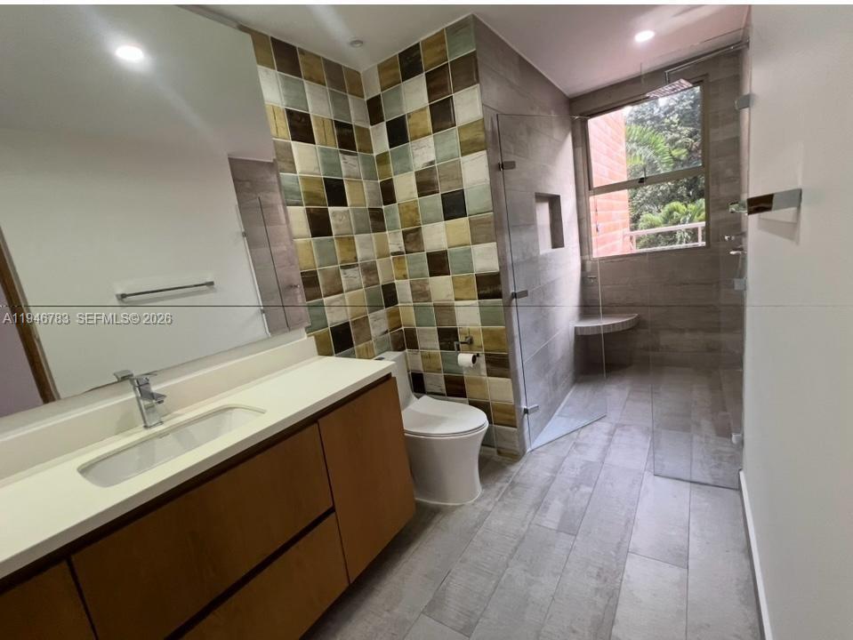 A modern bathroom features a wood vanity, a tiled accent wall, and a glass-enclosed shower — Calle 1 B Sur 38-90 # 202, FL