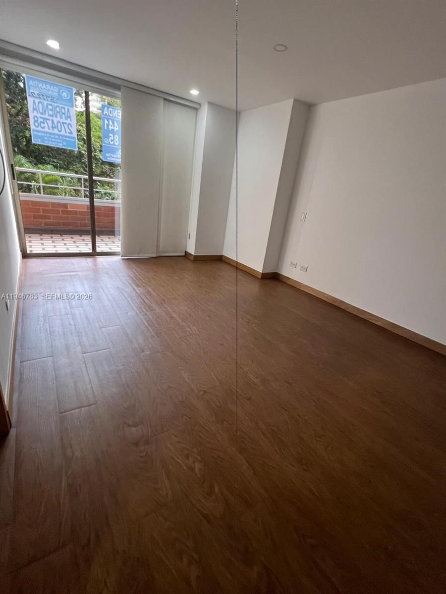 An empty room features wood-look flooring, white walls, a mirrored closet, and a sliding glass door — Calle 1 B Sur 38-90 # 202, FL
