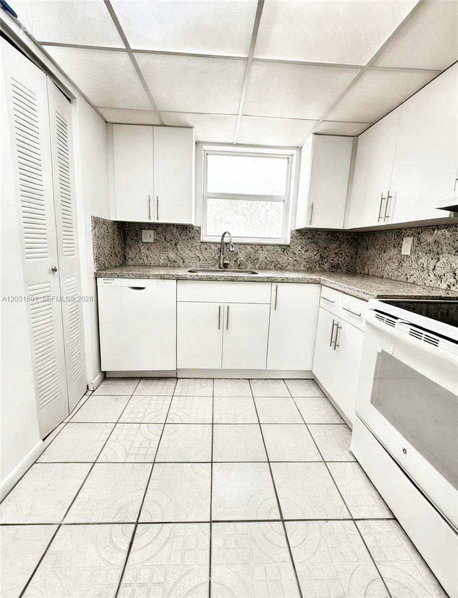 A kitchen features white cabinets, granite countertops, a white dishwasher, and tiled flooring — 13701 Kendale Lakes Cir # 308, Miami FL 33183, MIAMI, FL