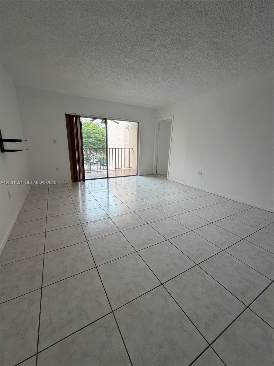 An empty room features white tiled floors, white walls, and a sliding glass balcony door — 13701 Kendale Lakes Cir # 308, Miami FL 33183, MIAMI, FL
