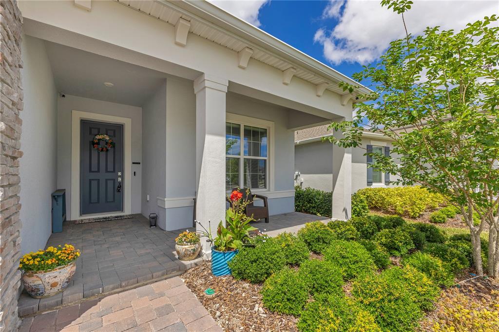 A covered front porch features a dark gray door, stone pavers, and landscaped garden beds — 13330 PANAMA BEACH COURT, ORLANDO, FL