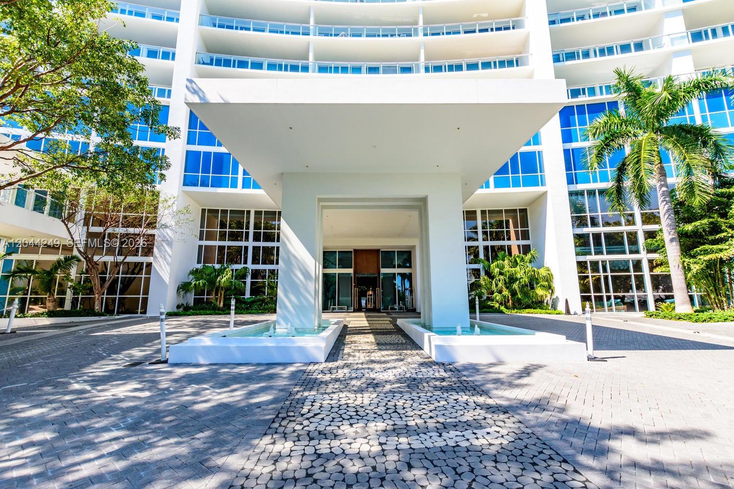 The exterior of a modern white building features a covered entrance with fountains and landscaping — 2020 N Bayshore Dr # 3904, Miami FL 33137, MIAMI, FL