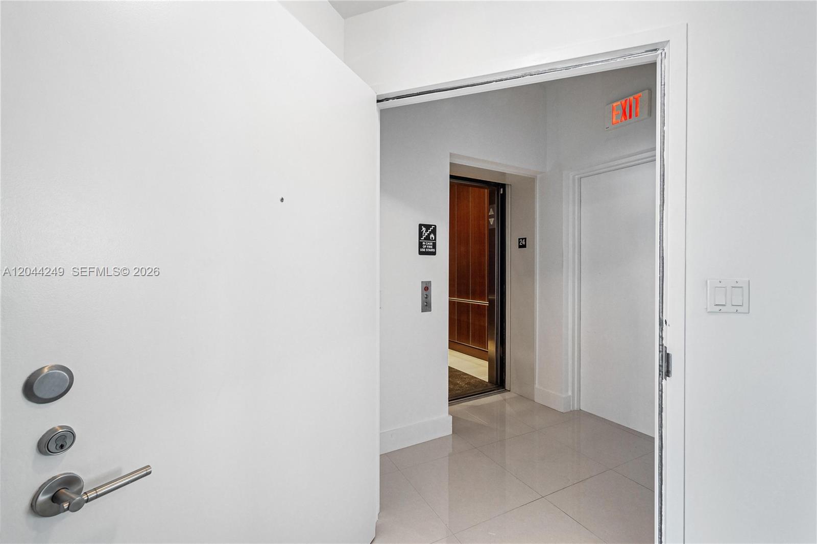 An open white door reveals a hallway with a tiled floor, an elevator, and an exit sign — 2020 N Bayshore Dr # 3904, Miami FL 33137, MIAMI, FL