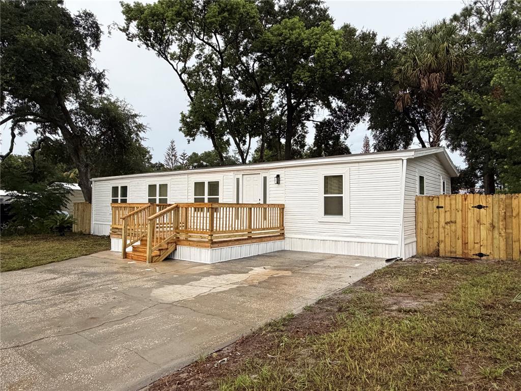 A white mobile home features a wooden deck and a concrete driveway under large trees — 791 N WINTER PARK DRIVE, CASSELBERRY, FL