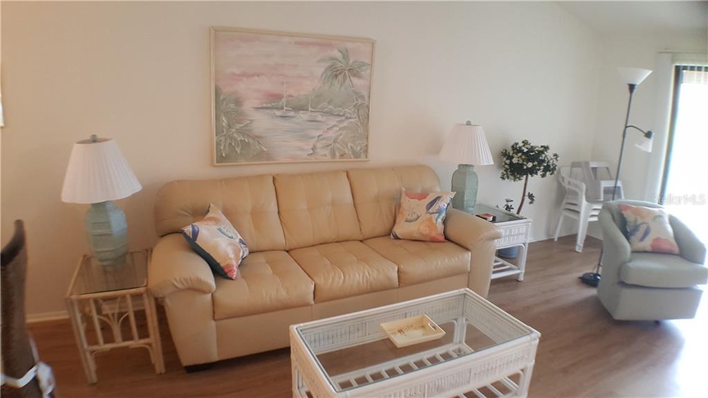 A living room features a beige leather sofa, a glass-topped coffee table, and coastal decor — 5907 36TH AVENUE CIRCLE W UNIT 5907, BRADENTON, FL