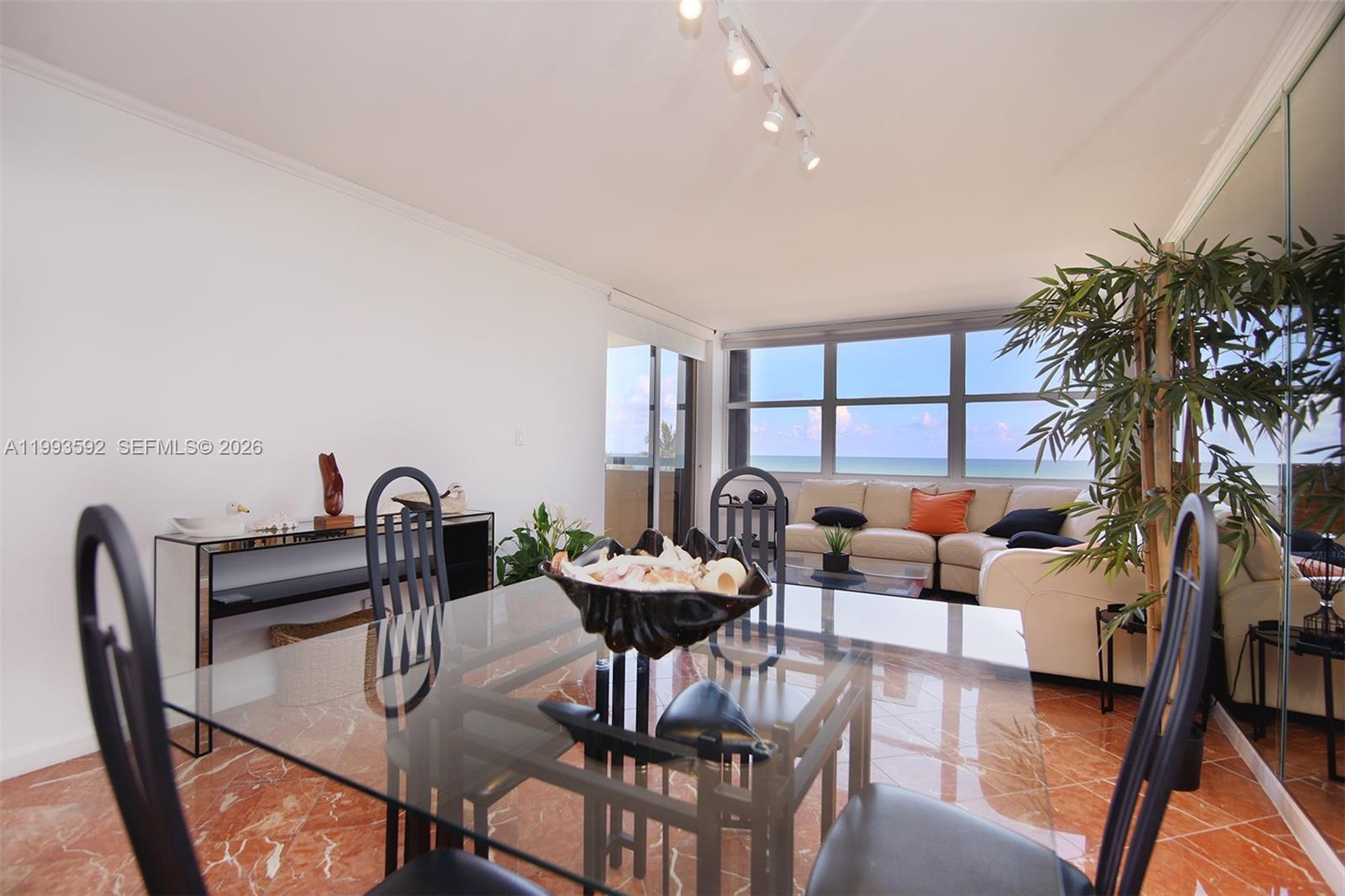 A dining area with a glass table and chairs overlooks a living room with ocean views — 2555 Collins Ave # 703, Miami Beach FL 33140, MIAMI BEACH, FL