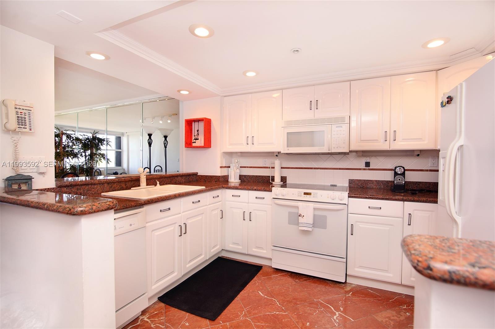 A kitchen features white cabinets, granite countertops, and red marble flooring — 2555 Collins Ave # 703, Miami Beach FL 33140, MIAMI BEACH, FL