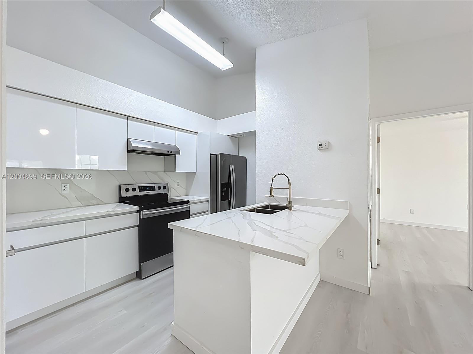 A modern kitchen features white cabinets, marble-patterned countertops, stainless steel appliances, and a peninsula sink — 2225 Metropolitan Way # 1225, Orlando FL 32839, ORLANDO, FL