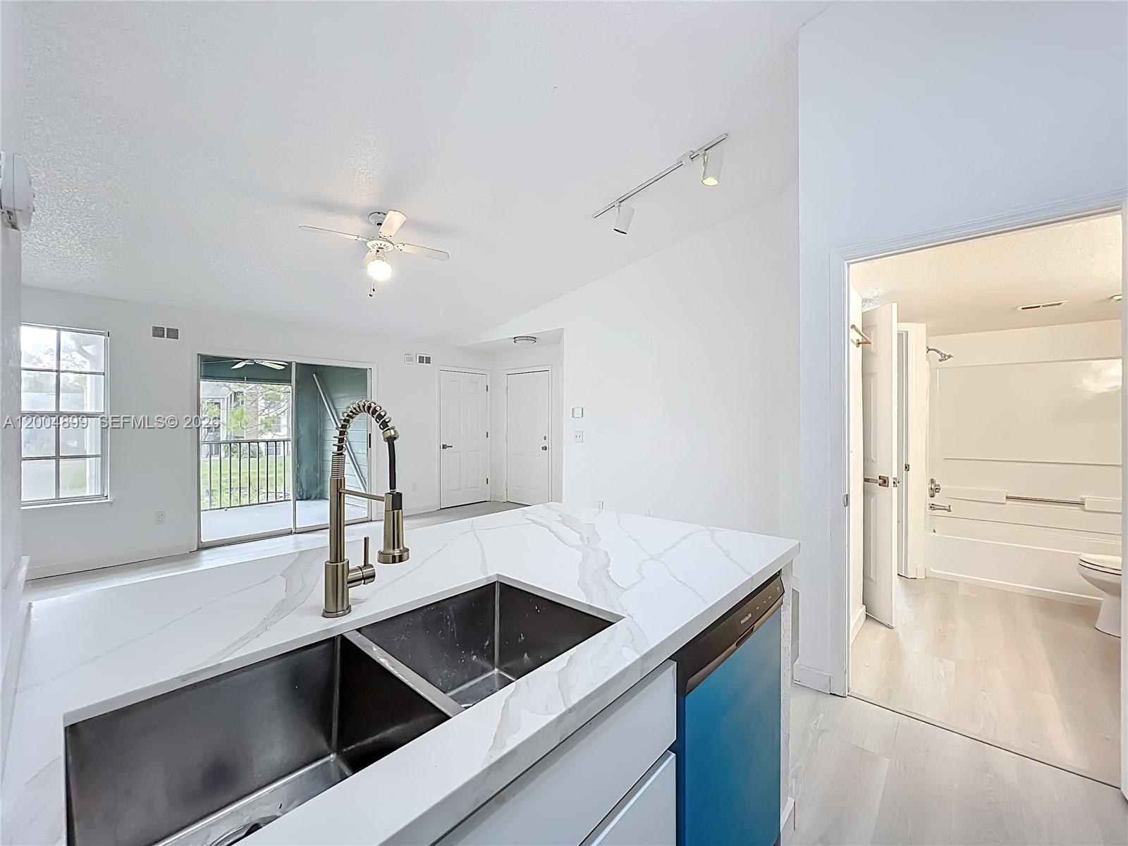 A kitchen island with a stainless steel sink overlooks a living area and a bathroom — 2225 Metropolitan Way # 1225, Orlando FL 32839, ORLANDO, FL