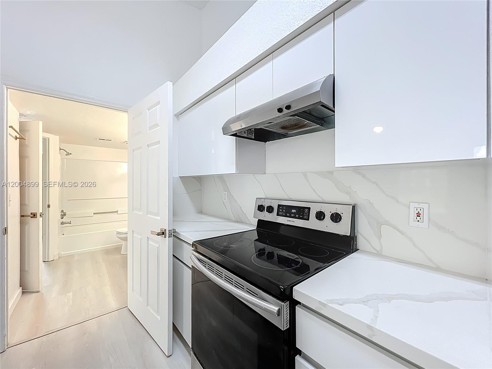 A kitchen with white cabinets and marble-look countertops leads into a bathroom with a tub — 2225 Metropolitan Way # 1225, Orlando FL 32839, ORLANDO, FL
