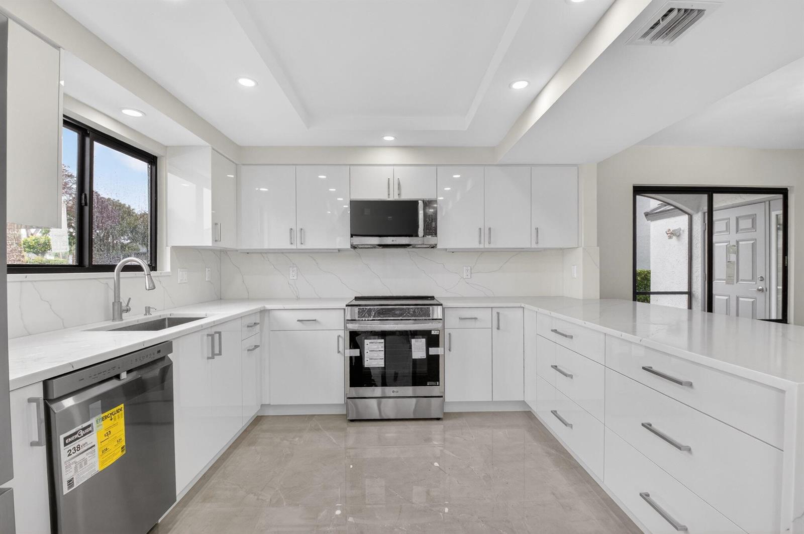 A modern kitchen features white glossy cabinets, stainless steel appliances, and white marble-patterned countertops — 15350 Strathearn Drive # 12501, Delray Beach FL 33446, DELRAY BEACH, FL