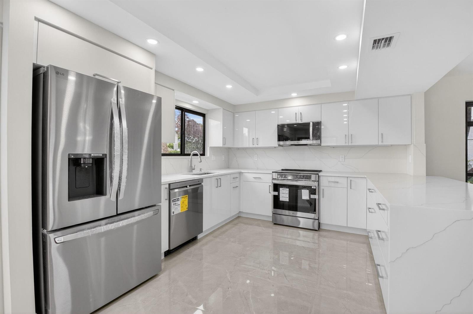 A modern kitchen features white glossy cabinets, stainless steel appliances, and light-colored marble-patterned countertops — 15350 Strathearn Drive # 12501, Delray Beach FL 33446, DELRAY BEACH, FL