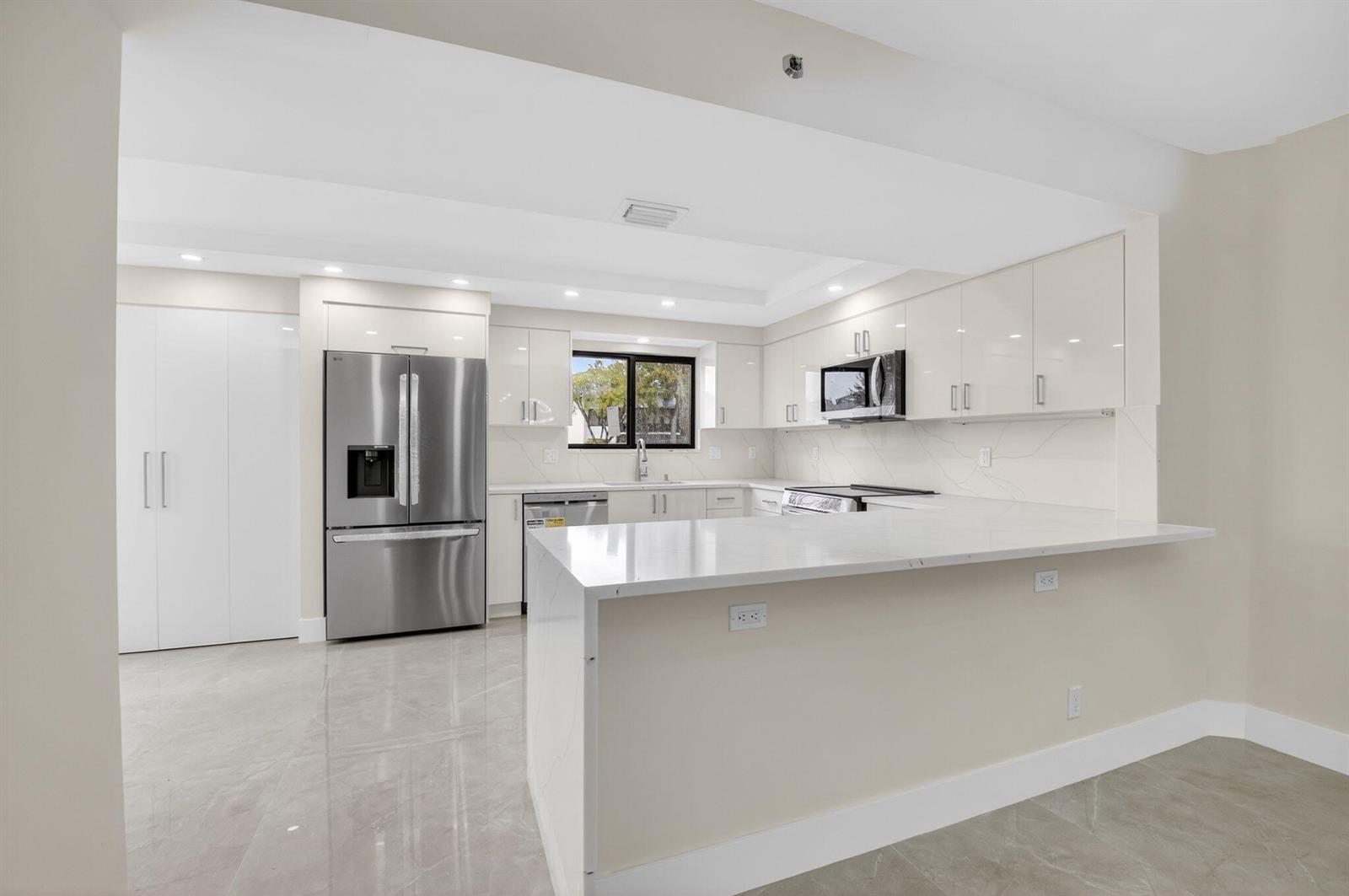 A modern kitchen features white glossy cabinets, stainless steel appliances, and a white quartz peninsula — 15350 Strathearn Drive # 12501, Delray Beach FL 33446, DELRAY BEACH, FL