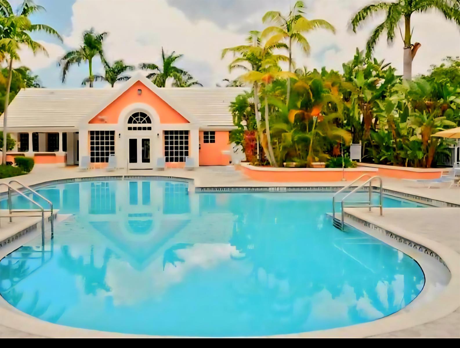 A peach-colored building with a white roof sits behind a large, clear swimming pool — 1020 Crystal Way # L, Delray Beach FL 33444, DELRAY BEACH, FL