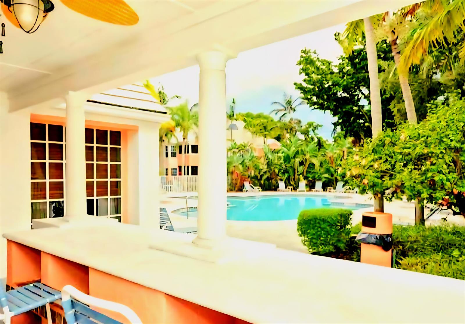 A covered patio with a bar overlooks a swimming pool surrounded by lush tropical landscaping — 1020 Crystal Way # L, Delray Beach FL 33444, DELRAY BEACH, FL