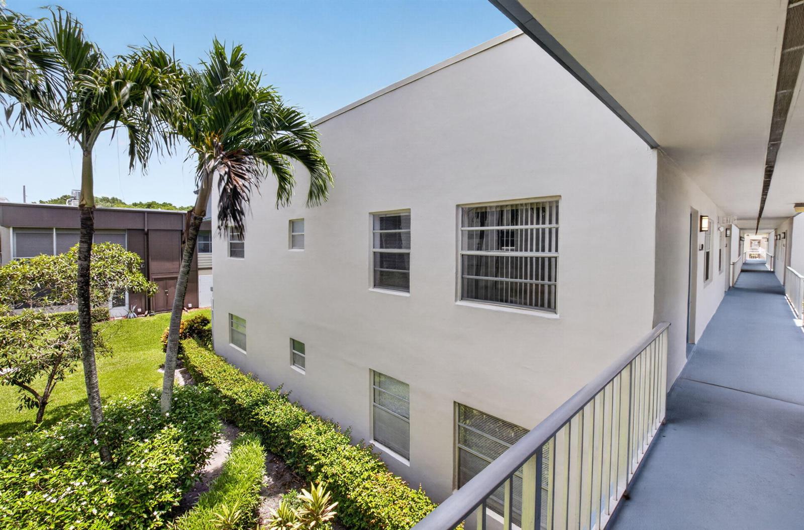 An exterior view of a multi-story apartment building with a walkway and palm trees — 809 Normandy Q # 809, Delray Beach FL 33484, DELRAY BEACH, FL