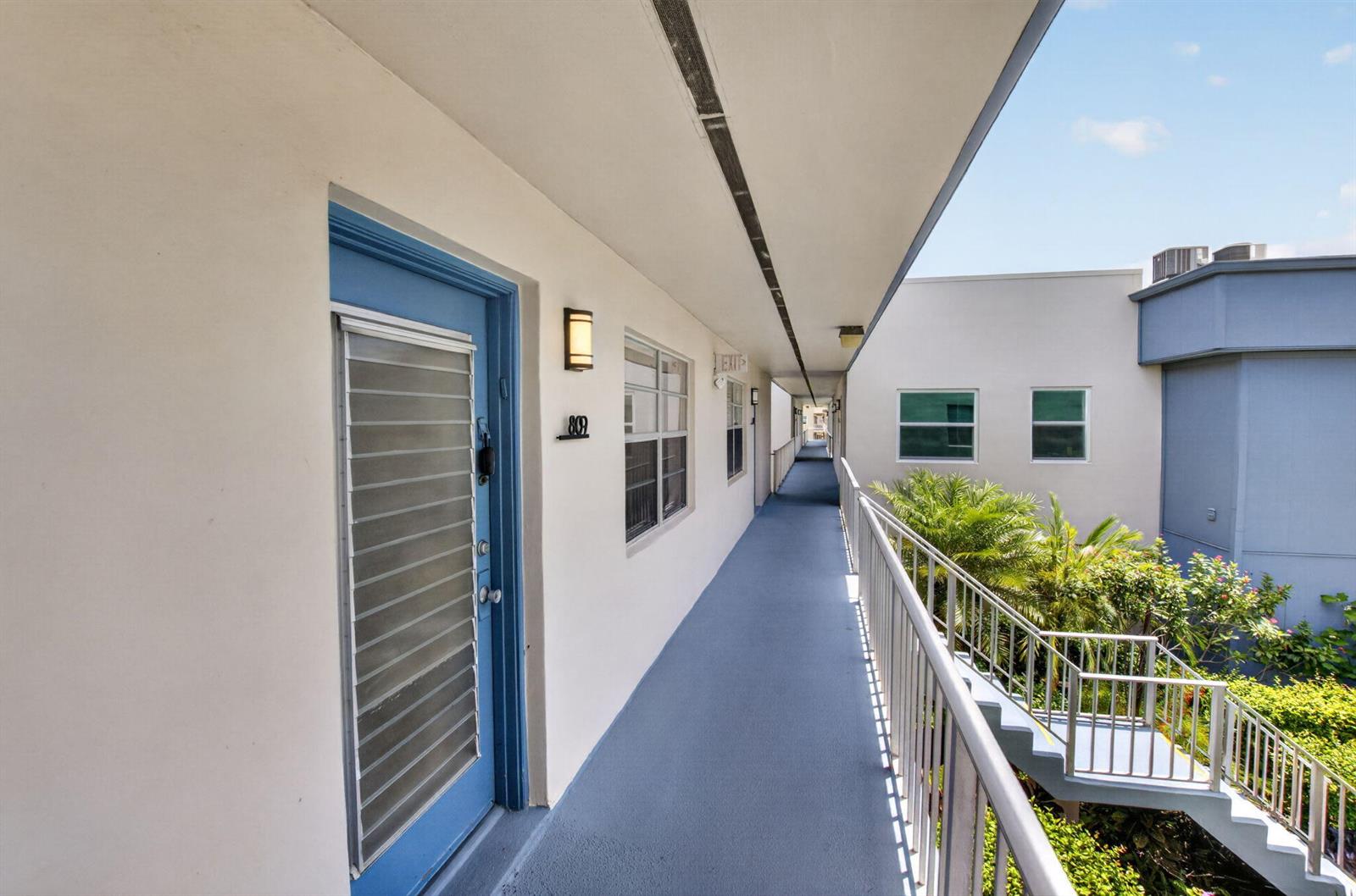 An outdoor walkway with blue flooring leads past a blue door labeled 809 — 809 Normandy Q # 809, Delray Beach FL 33484, DELRAY BEACH, FL
