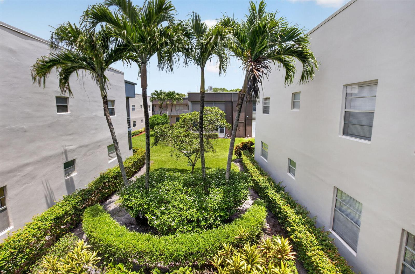 An exterior view of a grassy courtyard between two white apartment buildings with palm trees — 809 Normandy Q # 809, Delray Beach FL 33484, DELRAY BEACH, FL