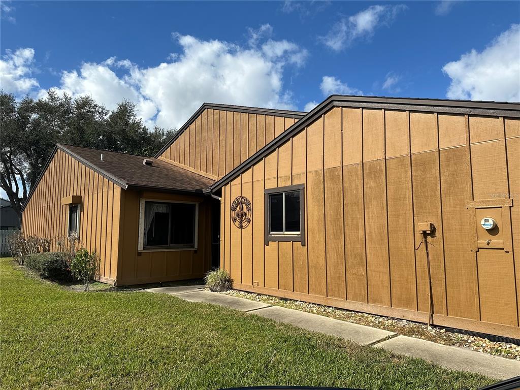 A single-story house with brown vertical wood siding and a concrete walkway in front — 156 LAKEWOOD VILLAGE CIRCLE, DAYTONA BEACH, FL