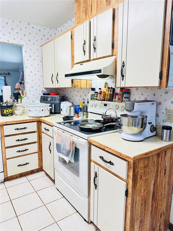 A kitchen features white cabinets with dark hardware, wood-grain trim, and a white electric stove — 156 LAKEWOOD VILLAGE CIRCLE, DAYTONA BEACH, FL