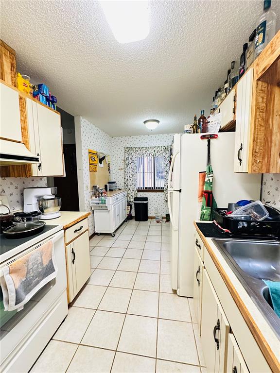 A galley kitchen features white cabinets, tile flooring, a white refrigerator, and a window — 156 LAKEWOOD VILLAGE CIRCLE, DAYTONA BEACH, FL
