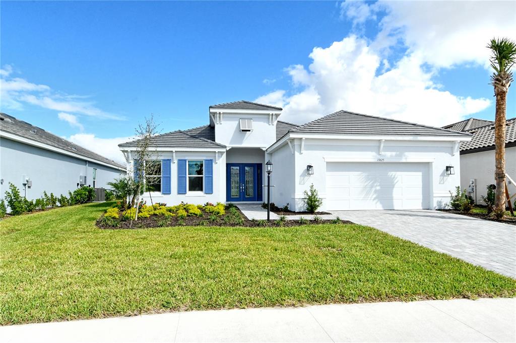A white single-story house with blue shutters, a tile roof, and a paved driveway — 15625 SAN LAZZARO AVENUE, BRADENTON, FL