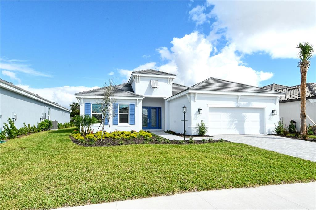 A white single-story house with blue shutters, a tile roof, and a two-car garage — 15625 SAN LAZZARO AVENUE, BRADENTON, FL