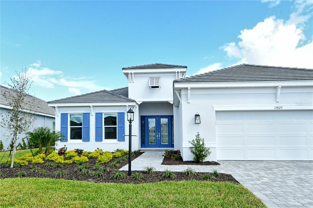 A white single-story house with blue shutters and a double front door under a blue sky — 15625 SAN LAZZARO AVENUE, BRADENTON, FL