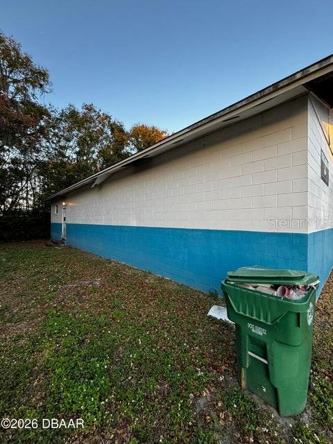A green trash bin sits on the grass beside the exterior of a concrete building — 227 W VOORHIS AVENUE, DELAND, FL