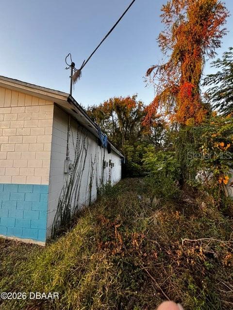 An exterior view of a light-colored block building with blue trim and overgrown vegetation — 227 W VOORHIS AVENUE, DELAND, FL