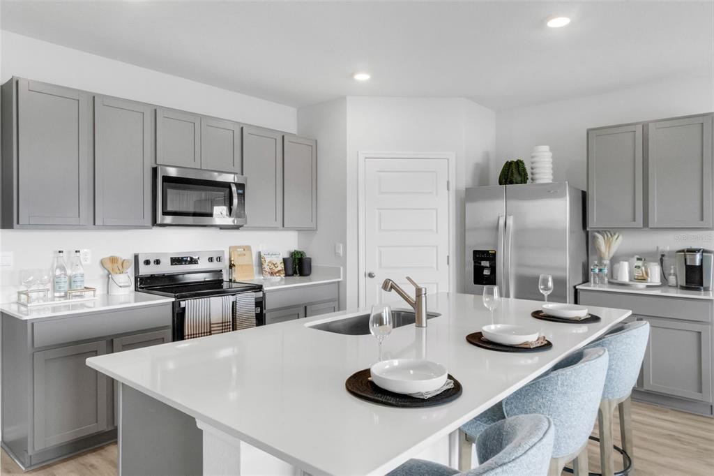 A modern kitchen features gray cabinets, white countertops, a central island, and stainless steel appliances — 1765 HUMMINGBIRD ROAD, WINTER HAVEN, FL