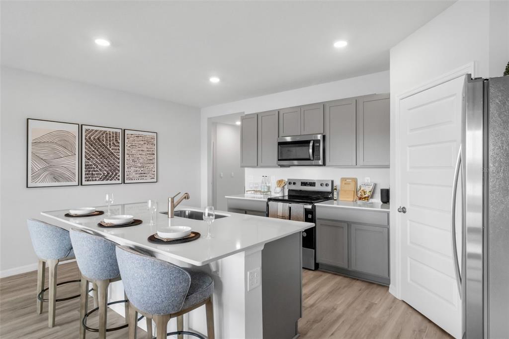 A modern kitchen features a white quartz island, gray cabinetry, and light wood-look flooring — 1765 HUMMINGBIRD ROAD, WINTER HAVEN, FL
