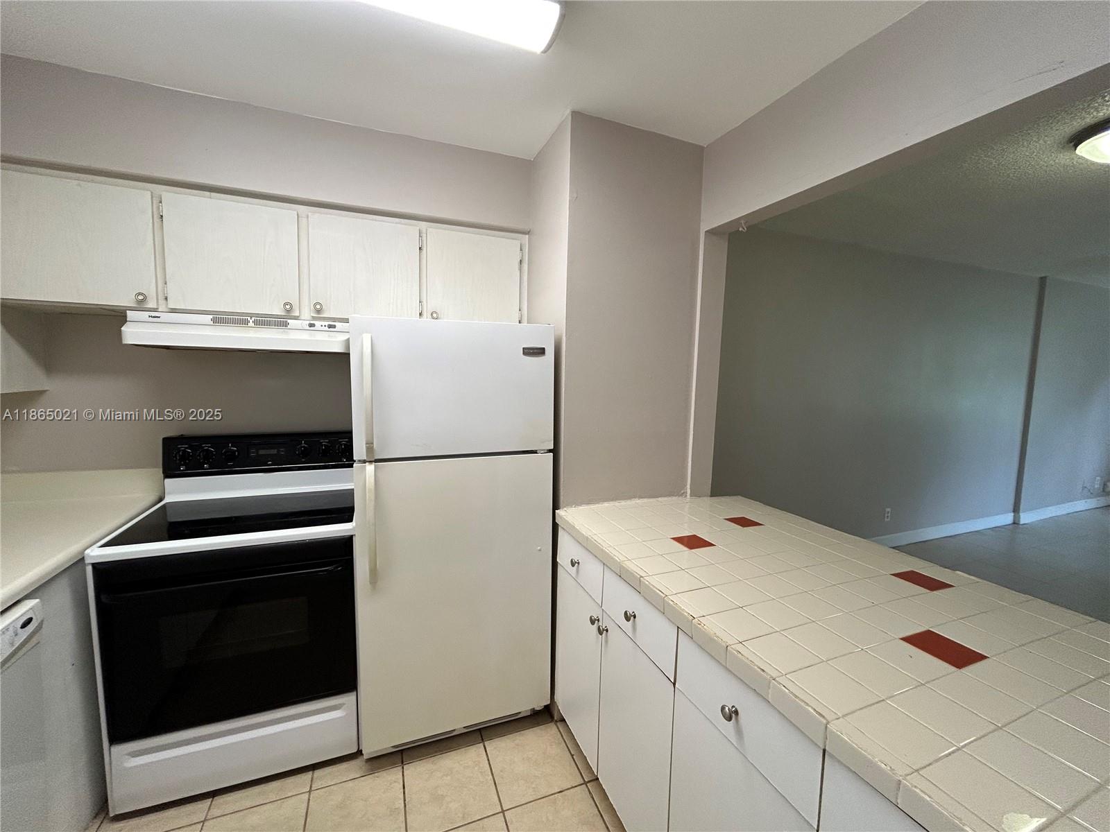 A kitchen features white cabinets, a white stove, a refrigerator, and a tiled countertop — 6505 Winfield Blvd # 18, Margate FL 33063, MARGATE, FL