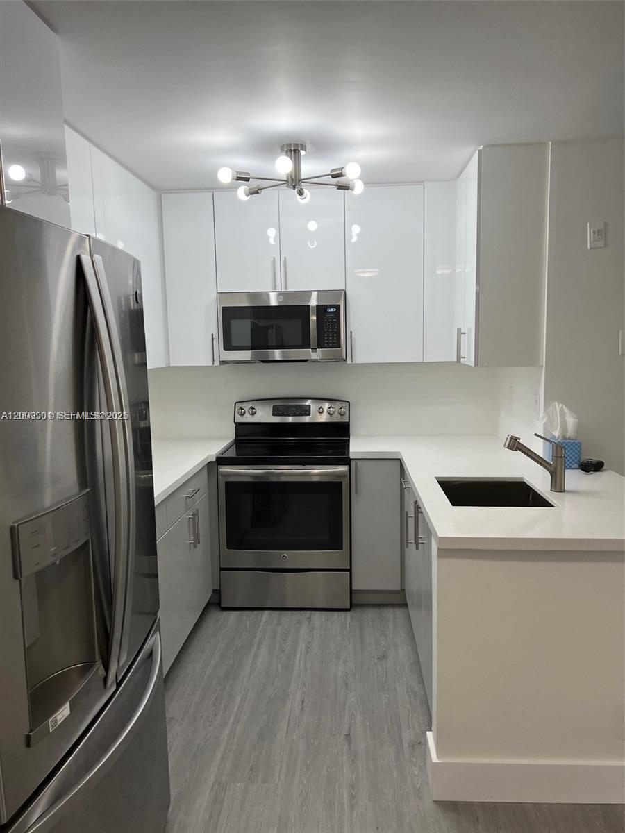 A modern galley kitchen features white high-gloss cabinets, stainless steel appliances, and quartz countertops — 931 Lyons Rd # 4101, Coconut Creek FL 33063, COCONUT CREEK, FL