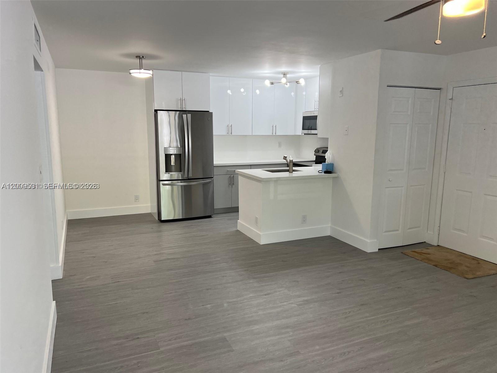 A modern kitchen features white cabinetry, stainless steel appliances, and gray wood-look flooring — 931 Lyons Rd # 4101, Coconut Creek FL 33063, COCONUT CREEK, FL