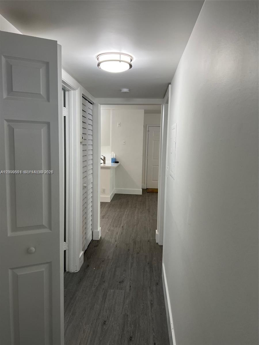 A hallway with gray wood-look flooring leads to a kitchen area with white cabinets — 931 Lyons Rd # 4101, Coconut Creek FL 33063, COCONUT CREEK, FL