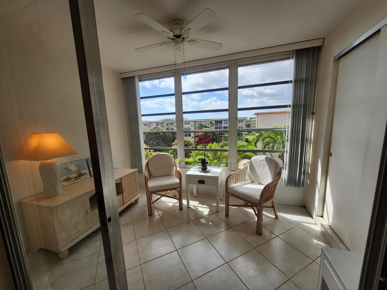 A sunroom features tile flooring, two wicker chairs, a small side table, and large windows — 230 NE 26th Avenue # 408, Boynton Beach FL 33435, BOYNTON BEACH, FL