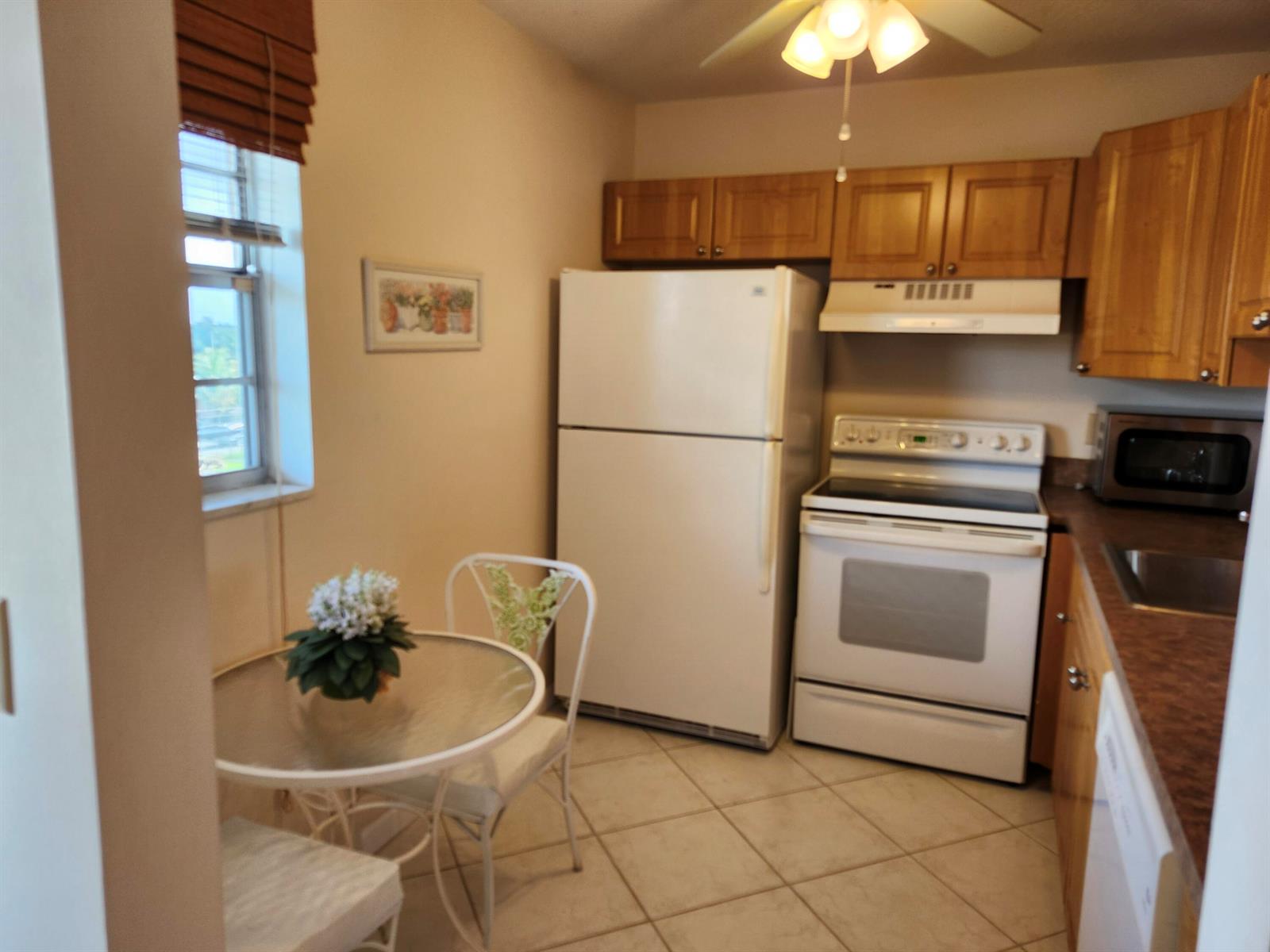 A kitchen features light-colored tile floors, wooden cabinets, white appliances, and a small dining table — 230 NE 26th Avenue # 408, Boynton Beach FL 33435, BOYNTON BEACH, FL