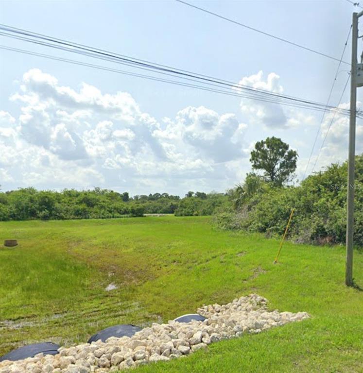 A grassy, undeveloped lot features a rocky drainage area in the foreground and dense vegetation — SAWYER CIRCLE, NORTH PORT, FL