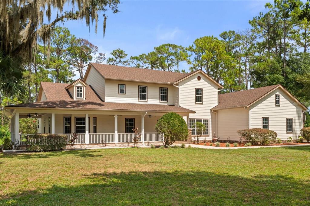 A two-story house with beige siding, a large covered porch, and a brown shingled roof — 27012 GRAND OAK LANE, TAVARES, FL