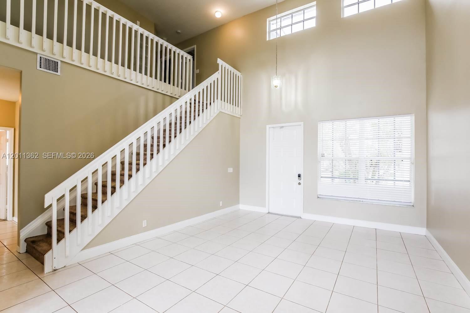 An entryway features a high ceiling, white tiled floors, and a staircase with white railings — PEMBROKE PINES, FL