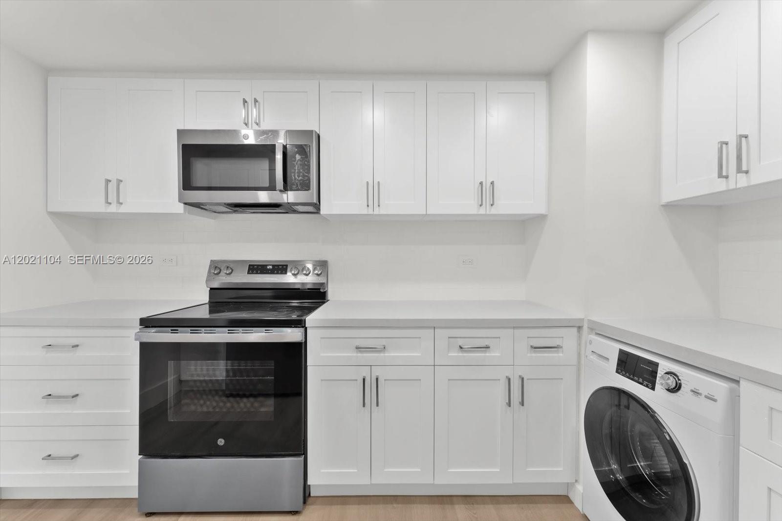 A kitchen features white cabinetry, a stainless steel microwave, a black oven, and a washer — 2451 Brickell Ave # 6N, Miami FL 33129, MIAMI, FL