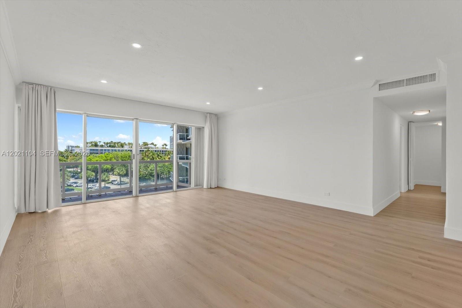 An empty room features light wood-look flooring, white walls, recessed lighting, and a sliding glass door — 2451 Brickell Ave # 6N, Miami FL 33129, MIAMI, FL