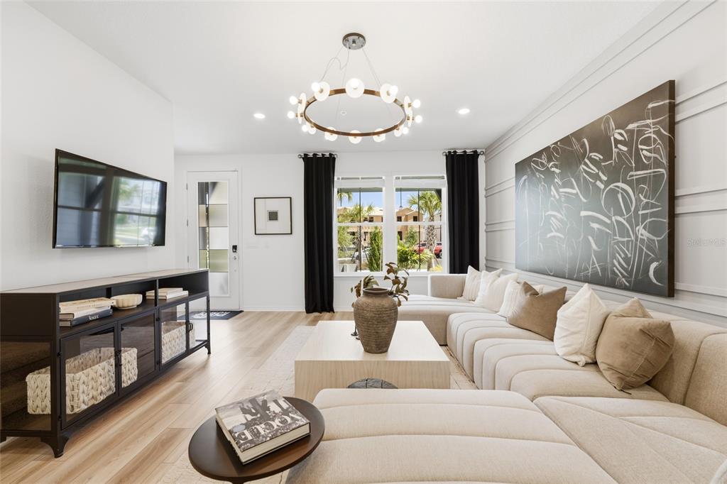 A modern living room features a large sectional sofa, a circular chandelier, and wall art — 4560 MAPLE WALTZ ALLEY, CLERMONT, FL